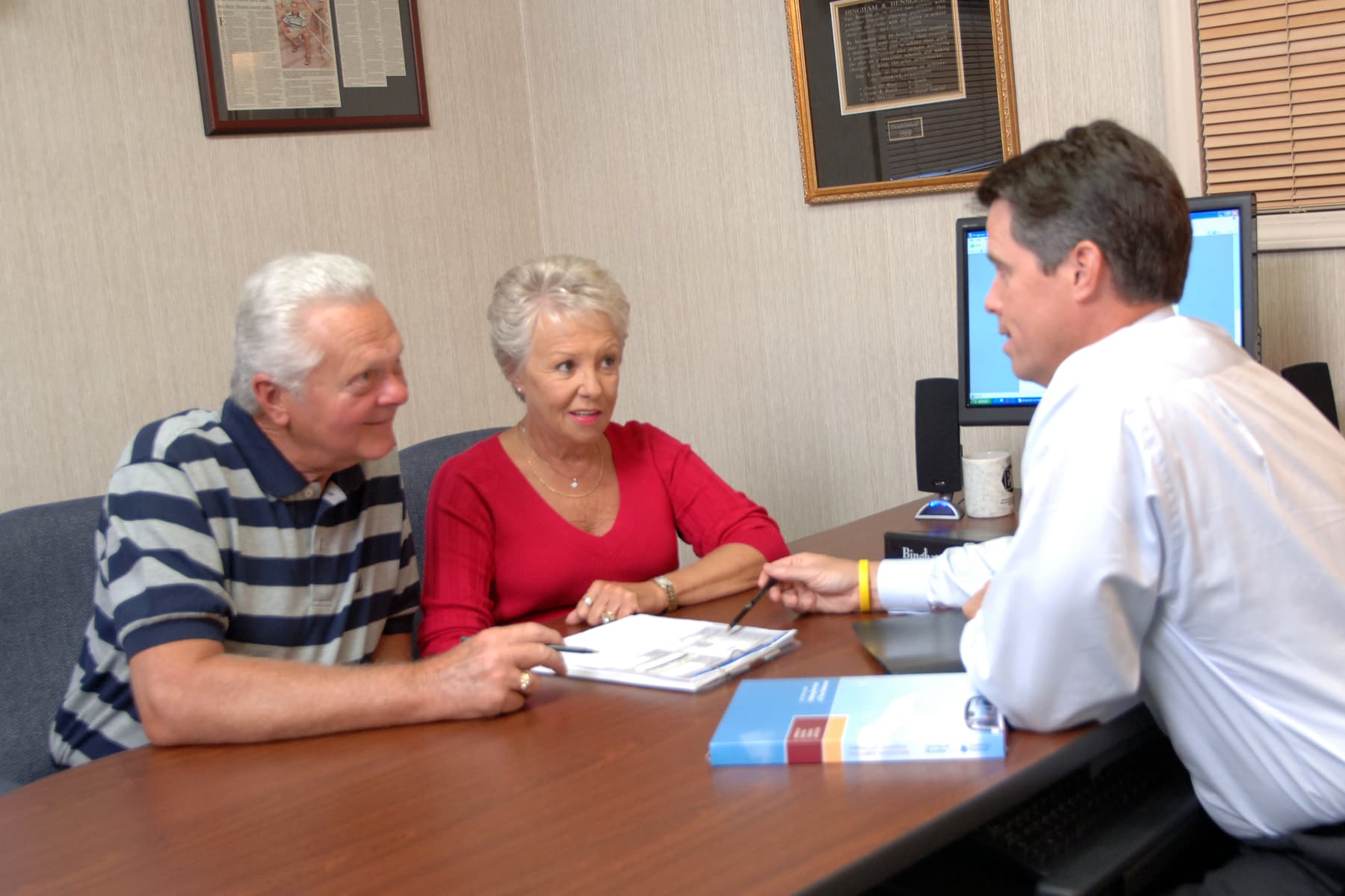 A retired couple sitting side by side at the conference table, going over a folder of paperwork with Jeff Bingham.
