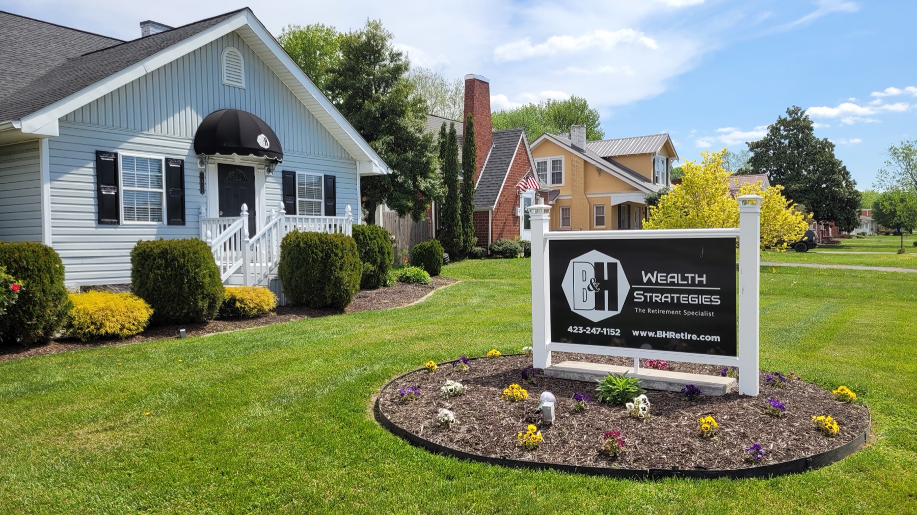 The B&H Wealth Strategies office in Kingsport: a pale blue clapboard house with a black awning over the door, and the firm's sign standing in the front lawn beside it